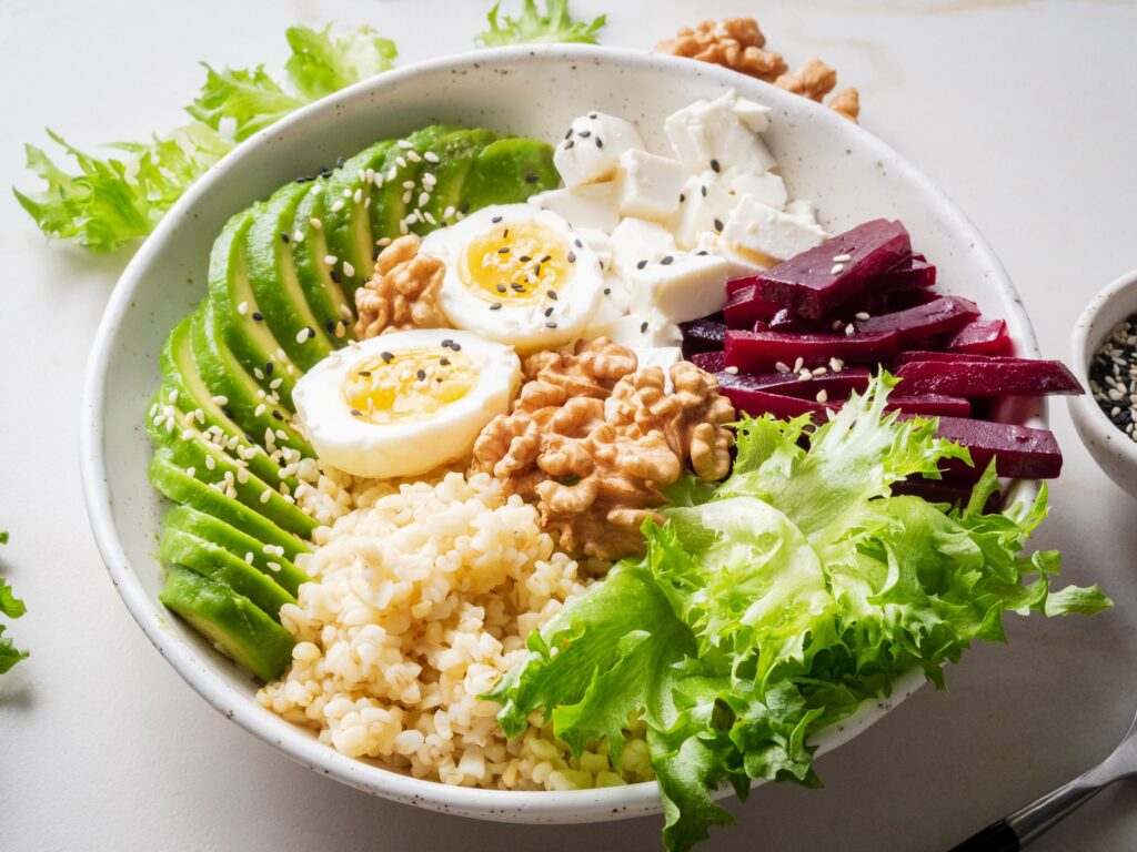 Vegetarian Buddha bowl. Grey marble table, side view. Eggs, avocado, salad lettuce, bulgur, beetroot, tofu.