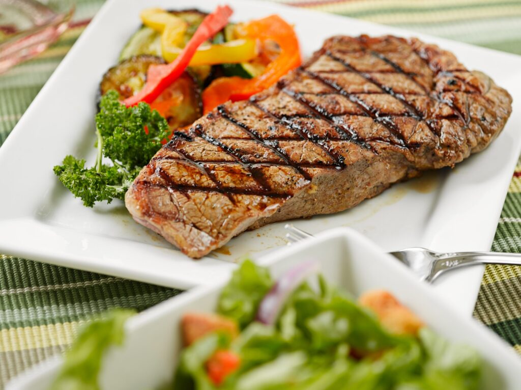 Grilled steak on a white rectangular plate with vegetables