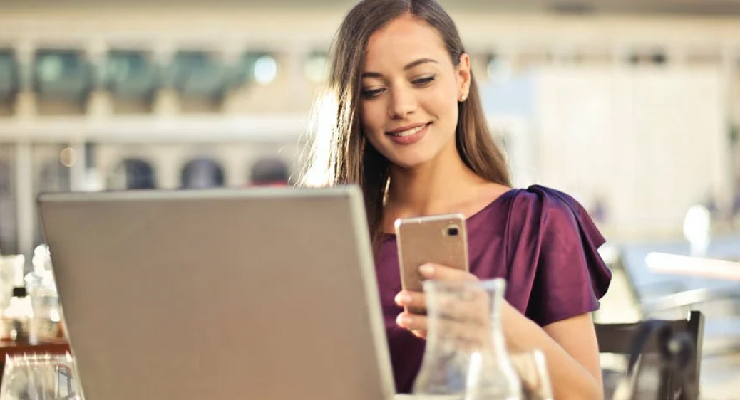 Woman looking at het phone while working on her laptop in a restaurant